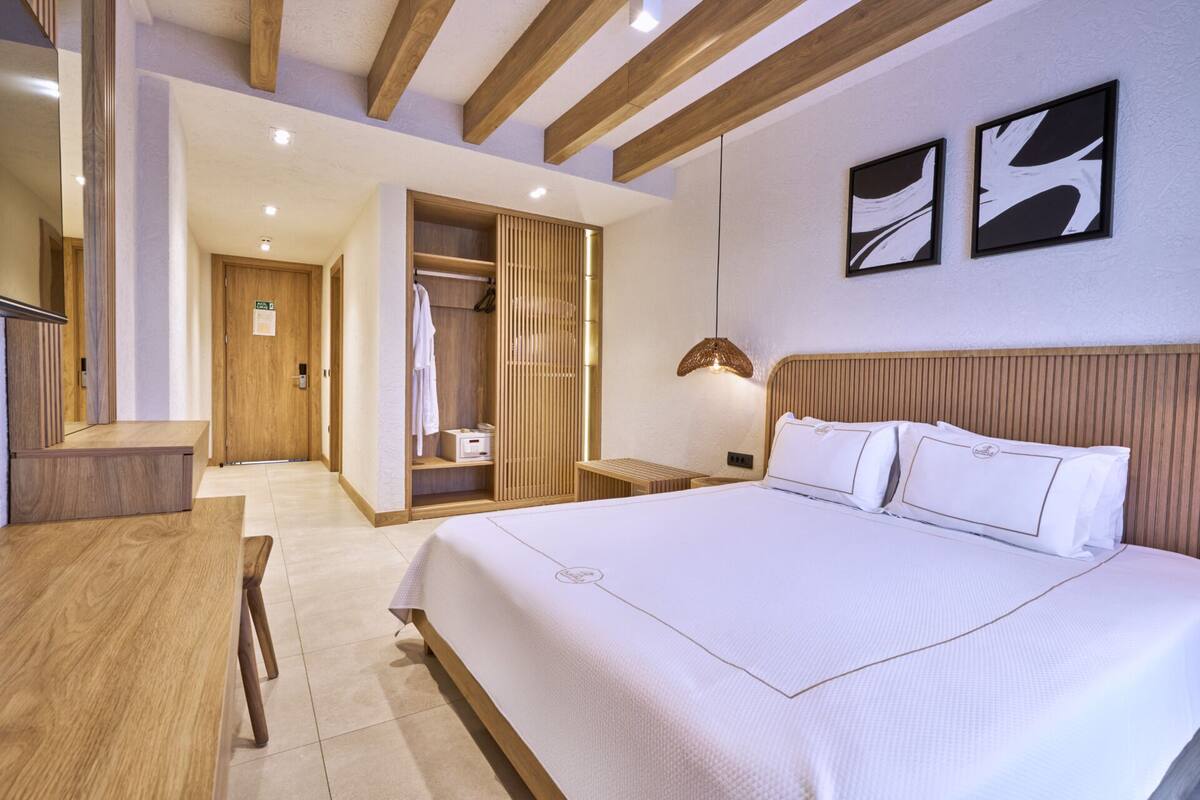 Une chambre d’hôtel avec un grand lit, une armoire en bois, un bureau et un espace douche.