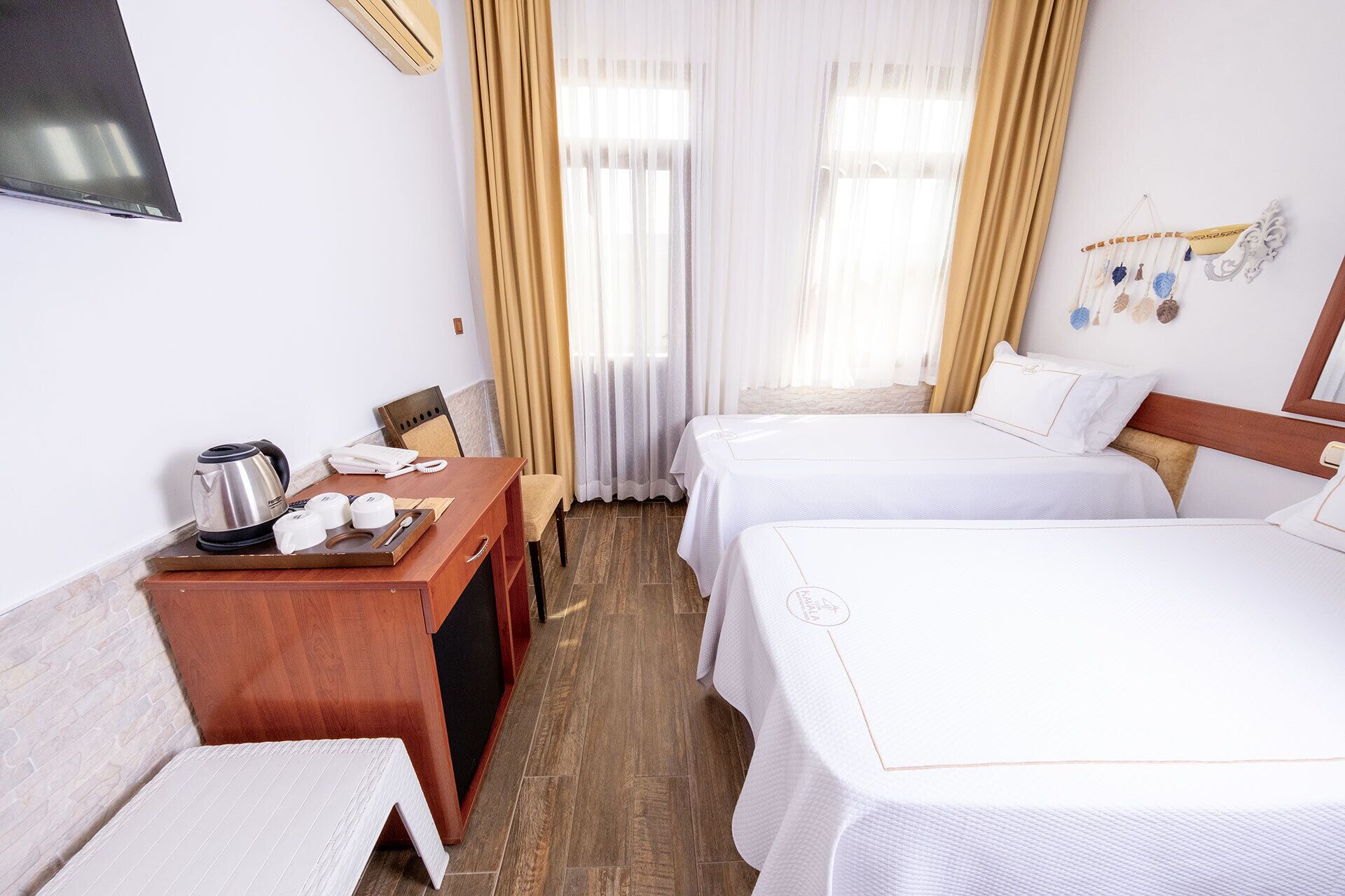 A hotel room with two single beds, a wooden desk with a kettle, a chair, and a small table with a tray.