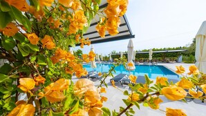 A pool area with lounge chairs and umbrellas, surrounded by greenery and yellow flowers. - Club Kavala Beach Hotel Assos (Ayvacik)