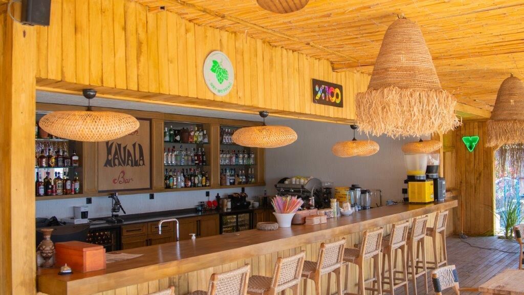 A wooden bar area with hanging wicker lamps, a minibar, and a sign for 'Kavala Bar'.