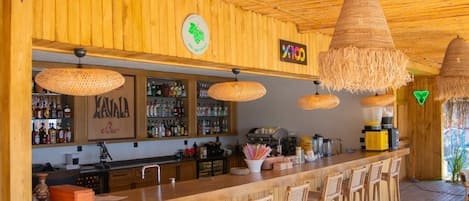 A wooden bar area with hanging wicker lamps, a minibar, and a sign for 'Kavala Bar'.