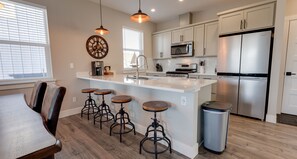 Une cuisine moderne dotée d’un îlot central, de tabourets de bar, d’appareils électroménagers en acier inoxydable et d’une grande fenêtre.
