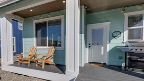 Een huis met een veranda, twee houten stoelen, een barbecue en een deur met een raam.