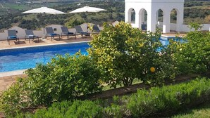 A pool area with a white gazebo, lounge chairs, and a view of the countryside.