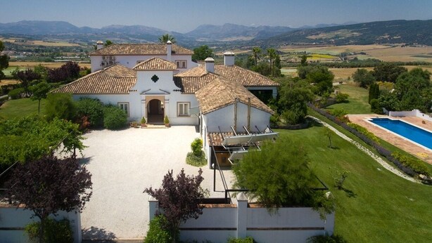 A large villa with a spacious driveway, a swimming pool, and a view of distant mountains.