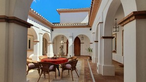 A courtyard with a round table and chairs, arches, and a tiled floor.