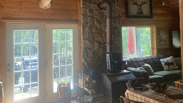 A rustic cabin interior with a stone fireplace, wooden ceiling, and a deer head mounted on the wall. - Beautiful Cabin in the woods  Allegany County NY (Belmont)