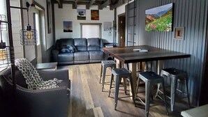 A spacious living area with a dark leather sofa, a wooden dining table with stools, and a ceiling fan. - Pikes Peak Views: One Block to Downtown (Woodland Park)