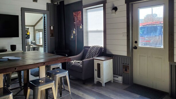 A dining area with a wooden table, bar stools, a dark upholstered chair, and a small white side table. - Pikes Peak Views: One Block to Downtown (Woodland Park)