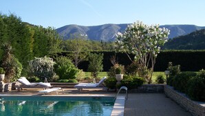 A pool area with lounge chairs, a stone wall, and a view of mountains. - Charm in Luberon (Ménerbes)