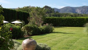 A well-maintained garden with a large decorative urn, neatly trimmed hedges, and a clear view of distant mountains. - Charm in Luberon (Ménerbes)