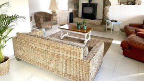 A cozy living room with a stone fireplace, wicker furniture, and a red leather sofa. - A traditional Breton vacation home near the sea (Roscoff)