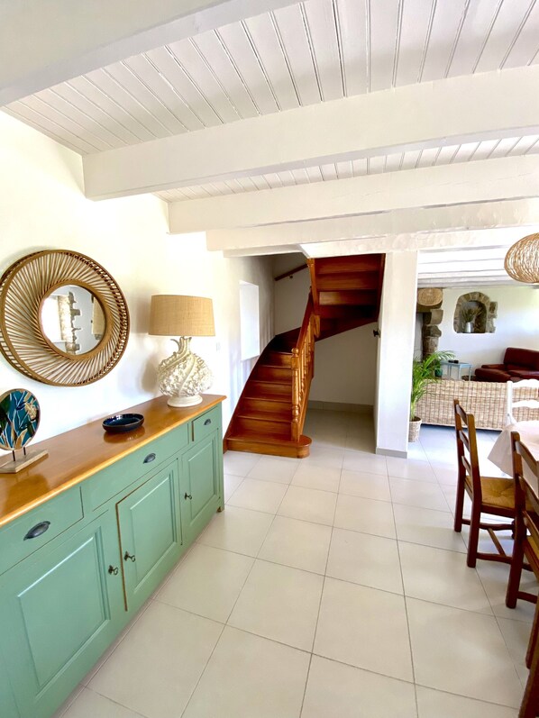 Una habitación amplia con una escalera de madera, un mueble de color aguamarina y una zona de comedor con sillas de madera.