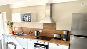 A modern kitchen with white cabinets, a stainless steel refrigerator, a built-in oven, a coffee maker, and a microwave. - A traditional Breton vacation home near the sea (Roscoff)