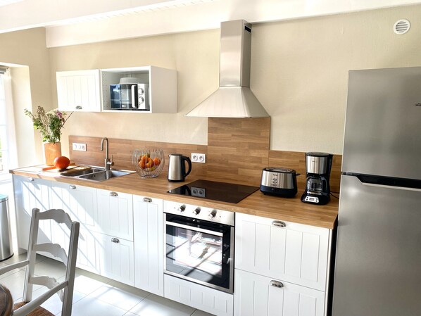 Una cocina moderna con armarios blancos, un refrigerador de acero inoxidable, horno empotrado, cafetera y microondas.
