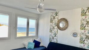 A room with a bed, a ceiling fan, a window with a view of the beach, and tropical wallpaper. - Waterfront studio, sea view 1st line beach (Palavas)