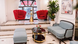 A modern lobby with two red armchairs, a blue sofa, and a glass coffee table with a vase of flowers. - Hồng Vận Hotel (Hanoi)
