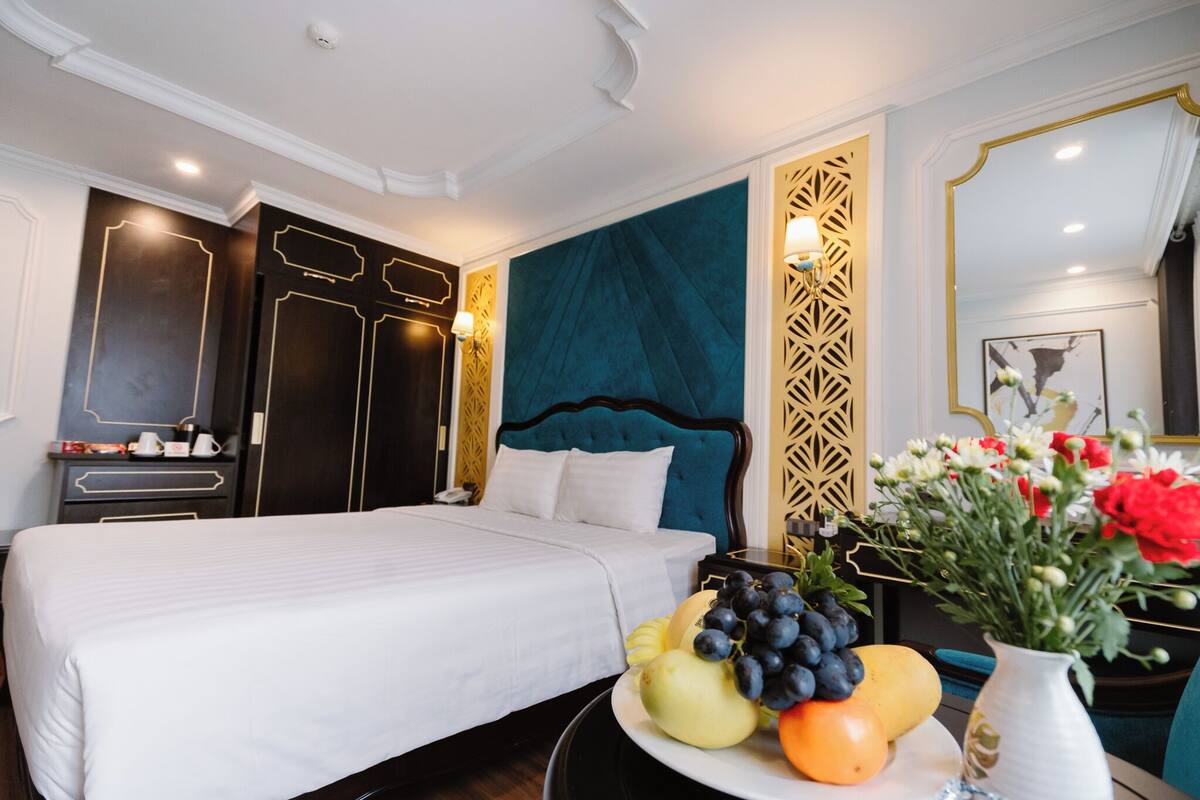 A hotel room with a large bed, a nightstand with a lamp, a wall with a geometric pattern, and a fruit bowl on the side table.