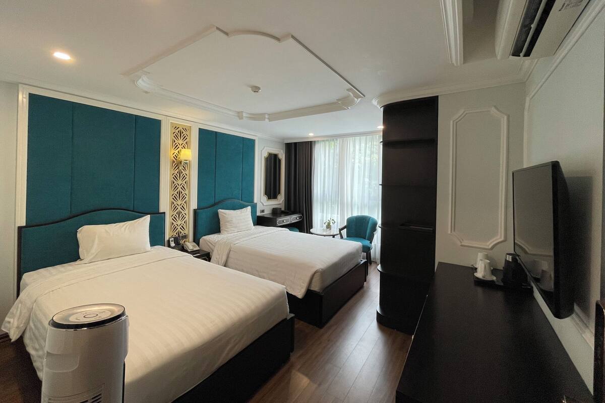 A hotel room with two beds, a desk, a chair, a TV, and a minibar.