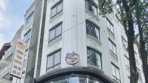A hotel entrance with a curved facade, a prominent logo, and a staircase leading to the entrance. - Hồng Vận Hotel (Hanoi)