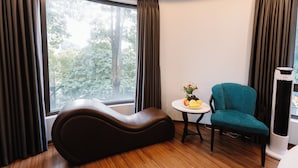 A modern room with a curved sofa, a small round table with fruit, a teal chair, and a standing heater. - Hồng Vận Hotel (Hanoi)