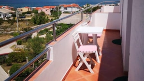 A balcony with a table and chairs, overlooking a coastal area with houses and mountains in the background. - Apartments Tara (Razanac)
