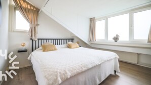 Un dormitorio con una cama grande, una ventana con cortinas, una mesita de noche con lámpara y un radiador.