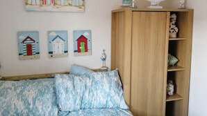 Ein Schlafzimmer mit einem Bett, einem Holzschrank und drei an der Wand befestigten Bildern von Strandhäusern.