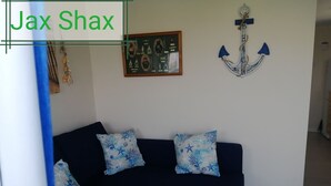 Ein Wohnzimmer mit einem dunkelblauen Sofa, zwei gemusterten Kissen, einem gerahmten Bild mit maritimer Motiven und einer Wanddekoration in Form eines Ankers.