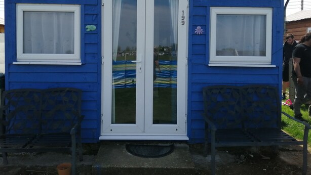 Ein kleines blaues Haus mit zwei Fenstern, einer Tür und einer Bank davor.