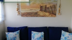 Ein Zimmer mit einem Strandbild, einem Holzzaun und einem blauen Sofa mit gemusterten Kissen.