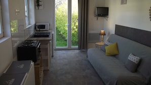 A compact bedroom with a bed, a bedside table with a lamp, a TV, and a kitchenette area with a microwave. - Studio on land "Countryside at the foot of MT ST MICHEL" (Roz-sur-Couesnon)