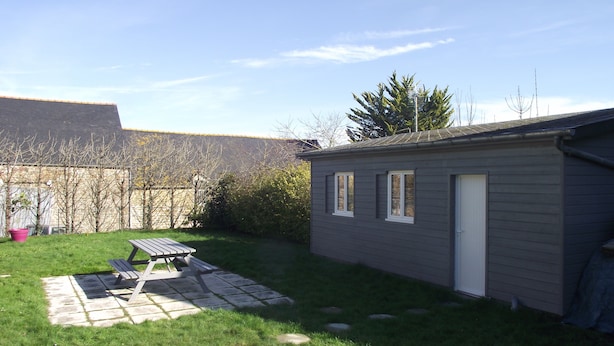 A small, single-story building with a door and windows, surrounded by a grassy yard with a picnic table. - Studio on land "Countryside at the foot of MT ST MICHEL" (Roz-sur-Couesnon)