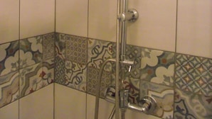A shower with a handheld showerhead and a wall-mounted faucet. The shower is enclosed by tiled walls with a decorative tile pattern at the bottom. - Studio on land "Countryside at the foot of MT ST MICHEL" (Roz-sur-Couesnon)