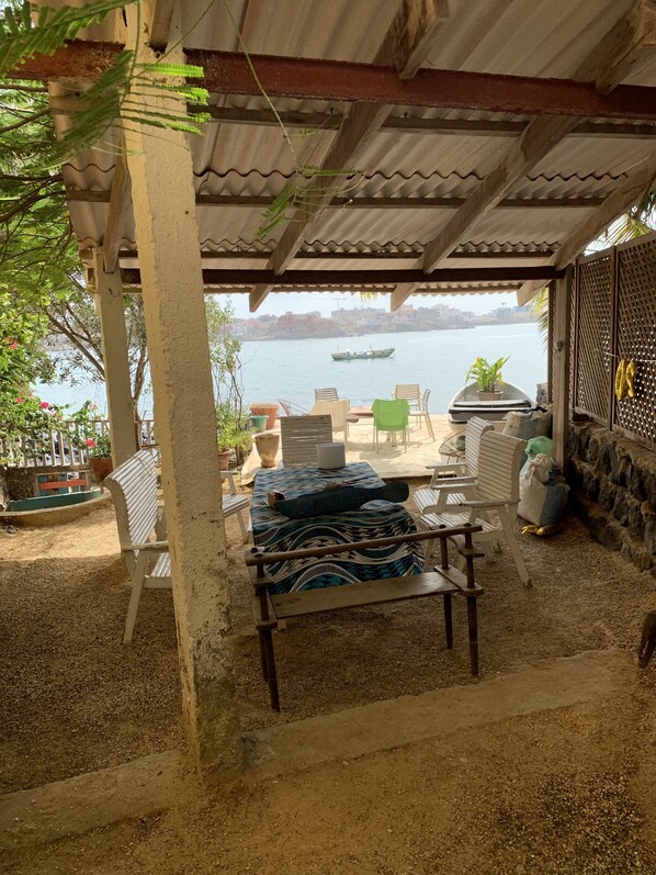 An outdoor seating area with a view of a river and a boat. There are chairs and tables, and a potted plant.