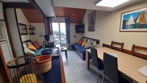 En kompakt opholdsstue med sofa, spisebord, fjernsyn og et billede på væggen.