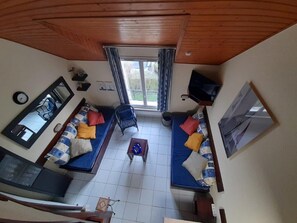A compact living room with two sofas, a small table, a TV mounted on the wall, and a window with curtains.