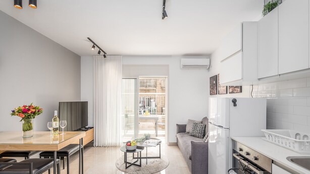 A modern kitchen with white cabinets, a dining area with a glass table, and a sofa. - Stylish one BDR with balcony (Jerusalem)