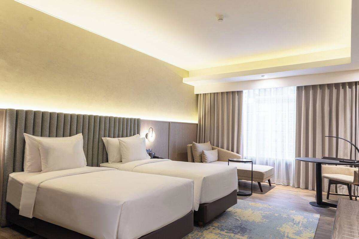 Een hotelkamer met twee bedden, een bureau, een stoel en een groot raam met gordijnen.
