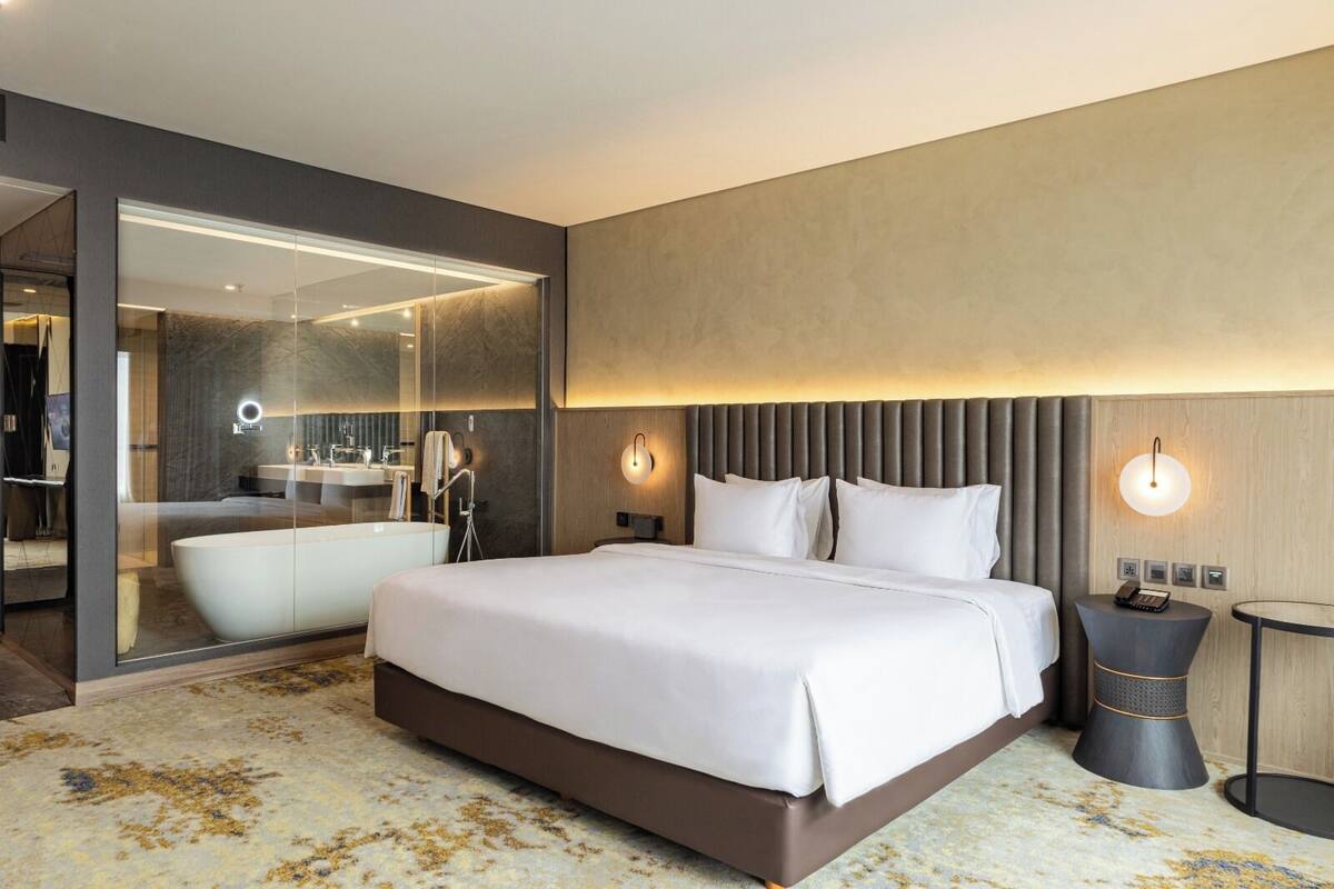 Een moderne hotelkamer met een groot bed, een aparte badkamer met een badkuip, een ronde tafel met een telefoon en een spiegel.