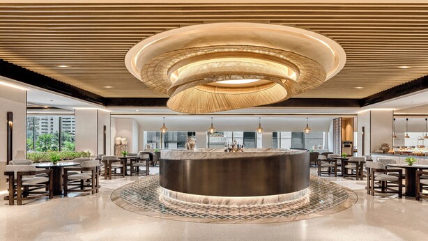 A modern lobby with a central circular bar, seating arrangements, and a large window providing a view of the outdoors. - Mangkuluhur ARTOTEL SUITES (Jakarta)