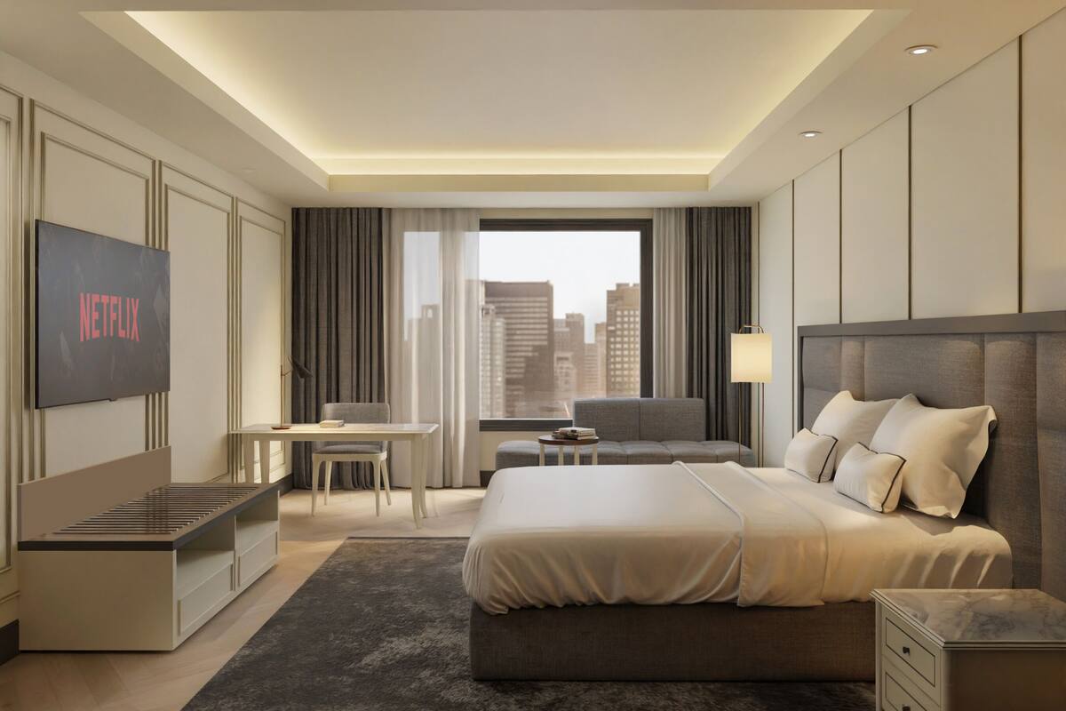 Een moderne hotelkamer met een groot bed, een bureau, een tv waarop 'NETFLIX' wordt weergegeven en uitzicht op de stad.