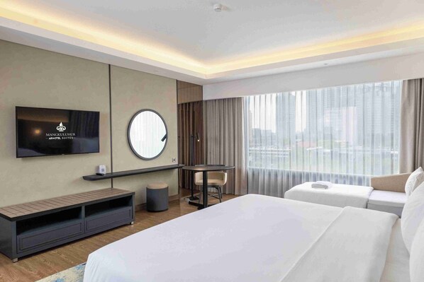 A modern hotel room with a large bed, a TV mounted on the wall, a round mirror, a small table, and a seating area with a view of the city.