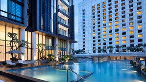 A modern hotel with a large indoor pool, lounge areas, and a view of the city skyline. - Mangkuluhur ARTOTEL SUITES (Jakarta)