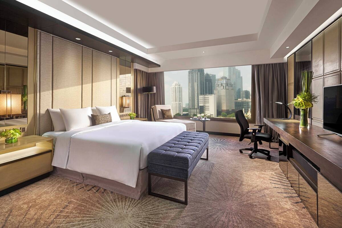 Een moderne hotelkamer met een groot bed, een bureau, een stoel en een televisie. De kamer heeft uitzicht op de stad en een groot raam.
