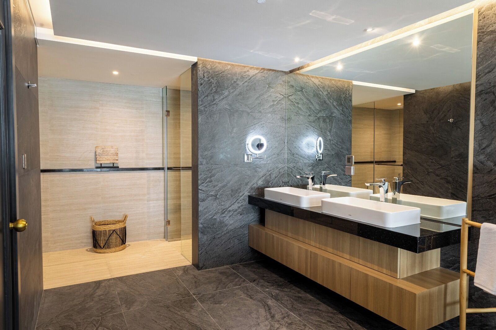 A modern bathroom with two sinks, a glass shower enclosure, and a large mirror.