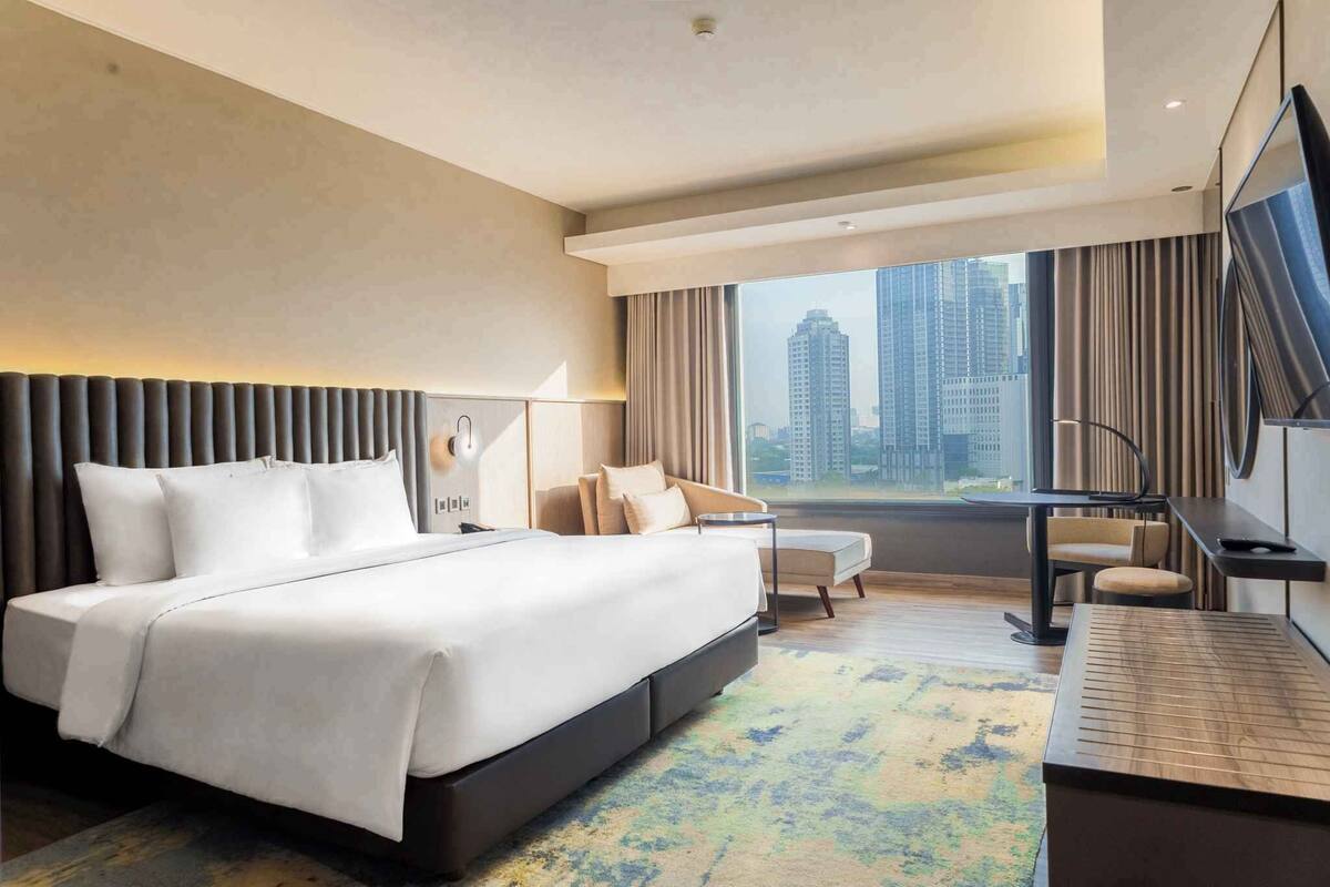 Een moderne hotelkamer met een groot bed, een bureau en uitzicht op hoge gebouwen.
