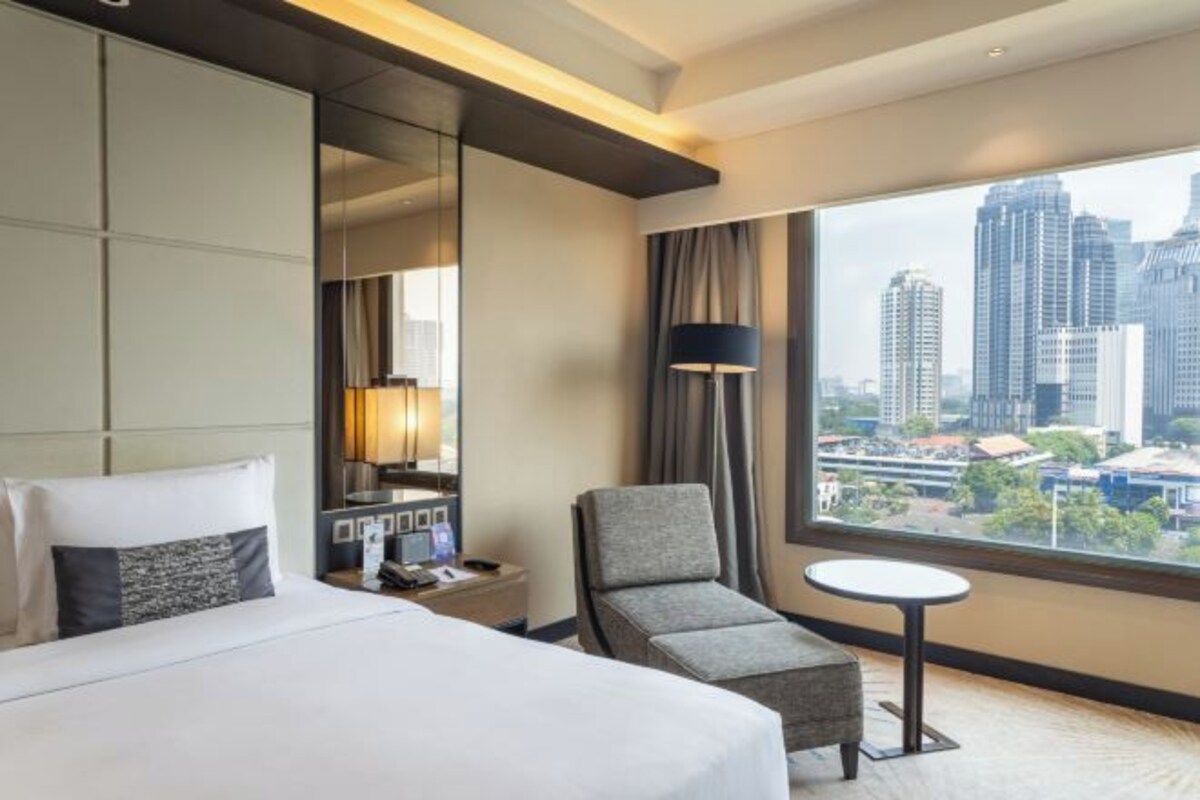 Een hotelkamer met een groot bed, een stoel, een tafeltje en uitzicht over de stad.