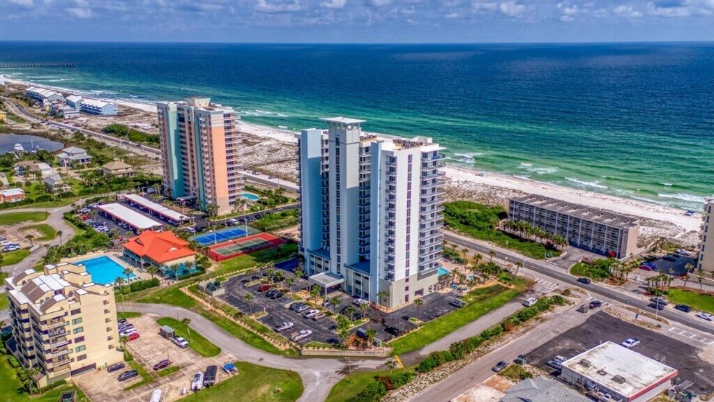 A coastal hotel with multiple high-rise buildings, a parking lot, and a beach view.