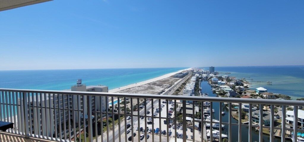 A coastal view from a balcony overlooking a beach, a marina, and a cityscape.